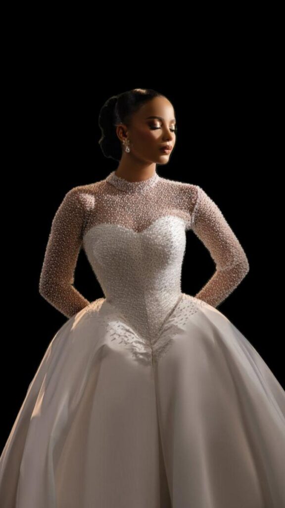 sculpted basque waist wedding gown featuring a beaded corset bodice, sheer long sleeves, and a full skirt, styled in a dramatic editorial bridal setting.